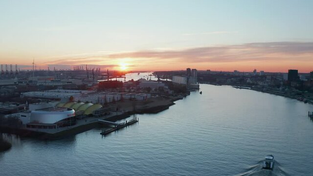 Aerial dolly out view of a boat driving along Elbe river past warehouses in industrial district of Hamburg port