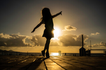 Happy dancing little girl watching the sunset near the beach