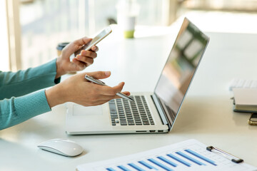 Close up Business woman using smartphone calculator and laptop for do math finance on wooden desk,...