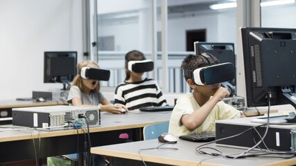 Multiethnic kids having fun using virtual reality headset. Funny blonde girl fooling and eating computer mouse. Children sitting and looking around. VR technology in education concept. - Powered by Adobe