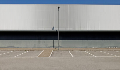Exterior wall made of gray concrete in the lower side and aluminium cladding in the upper with a street light. Porphyry sidewalk, parking and asphalt road in front. Background for copy space © luca piccini basile