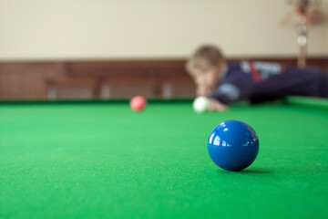 Teenager is playing snooker. Red balls are in the foreground.