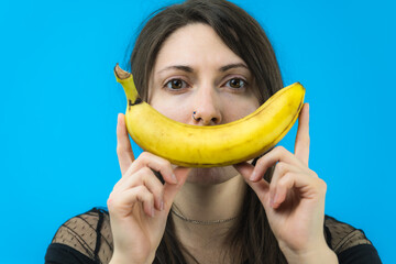 Giovane e bella ragazza si diverte creando un sorriso con una banana su sfondo blu