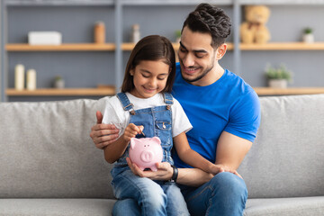 Little girl and dad saving money in piggy bank