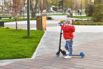 A little girl is riding a scooter on the sidewalk path in the park.