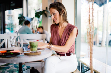 Beautiful caucasian female journalist working in cafe interior reding news and making research online, prosperous pretty woman watching video and checking mail on laptop computer on remote job