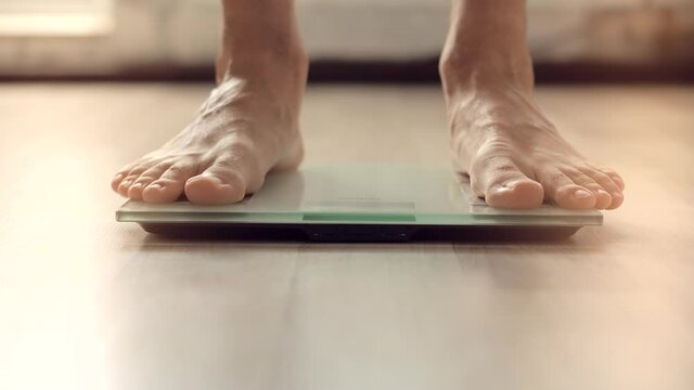 Man On Scales Measure Weight.Guy Legs Step On Bathroom Scale.Diet Man Feet Standing Weighing Scales On Room.Walking Male Checking BMI Weight Loss.Human Barefoot Measuring Body Fat Overweight.