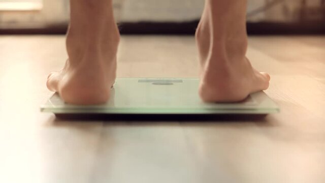 Man On Scales Measure Weight.Guy Legs Step On Bathroom Scale.Diet Man Feet Standing Weighing Scales On Room.Walking Male Checking BMI Weight Loss.Human Barefoot Measuring Body Fat Overweight.