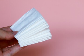 Stack of white pure natural cotton pads rolled edges for cleansing skin , hold in hand on pink background.