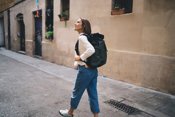 Caucasian female tourist with travel backpack walking around historic quarter enjoying solo vacations, casual dressed woman 30 years old exploring city streets during international excursion in town