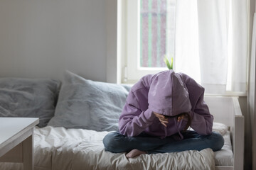 Full length stressed young teenage child girl sitting on bed, covering head with hands, suffering...