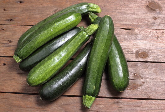 Gruppo di zucchine verdi disposti su tavole di legno grezzo.