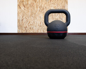 Naklejka na ściany i meble 20Kg black kettlebell isolated on the floor at the gym. Bodybuilding and fitness equipment with wooden wall protection board in the background. Empty space for text