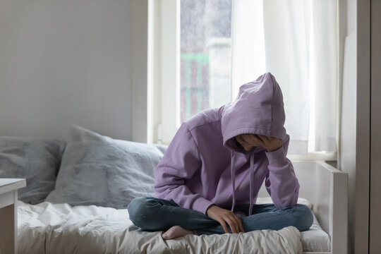 Unhappy young adolescent 12s kid girl sitting on comfortable bed, feeling exhausted or depressed alone at home. Stressed teen child suffering from headache or having psychological mental problems.