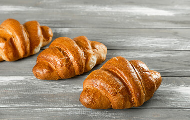 Three fresh French croissants on a wooden gray background.