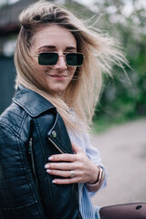 Young blonde in leather jacket and sunglasses posing in the street