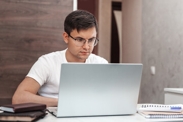 Focused man in glasses working at home with laptop