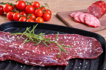 raw meat flecked with coarse salt and rosemary sprig on a cast iron plate