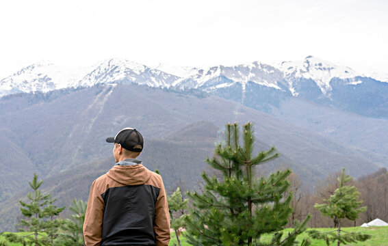 young man in cap from behind among the pine trees looking view of snow capped peak Caucasus mountains, travel, mountain landscape