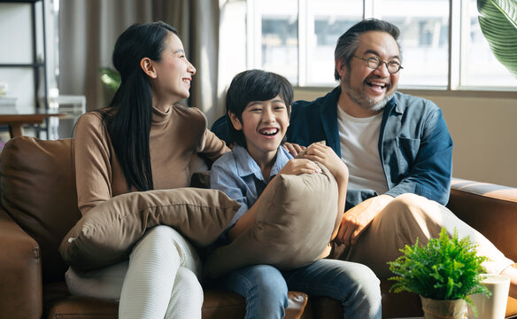 Happy Asian Family Spending Time By Watching Tv Together On Sofa In Living Room. Family And Home Concept