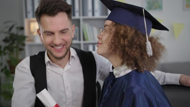 graduation, happy female student in mantle and hat hugs man and rejoices at received certificate of education online by video conference