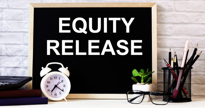 The words EQUITY RELEASE is written on the chalkboard next to the white alarm clock, glasses, potted plant, and pencils in a stand.