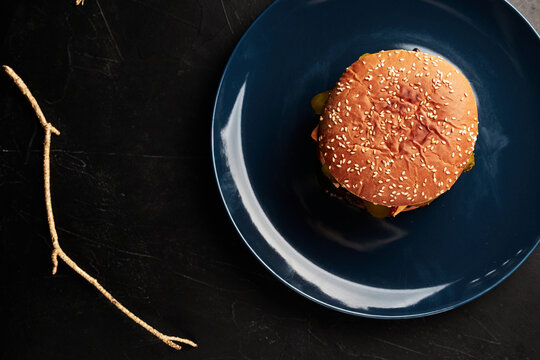 burger on a blue plate on a black background with a golden twig overhead view