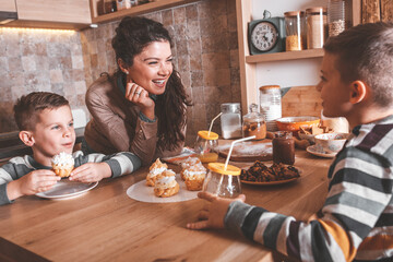 Mother and her two little sons eating cakes at the kitchen.Laughing and making fun.	