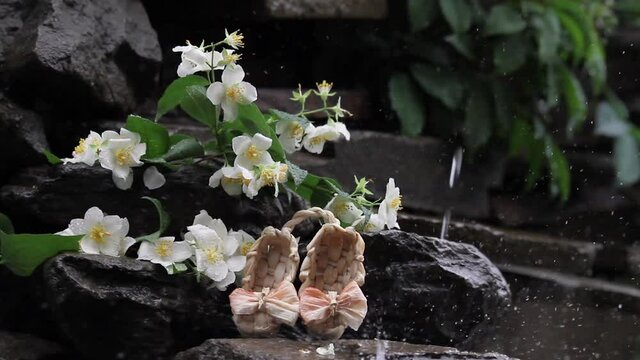 A bouquet of jasmine lies on the stones in the rain. Decorative bast shoes on the background of jasmine. Rainy day. Zooms in on the frame.