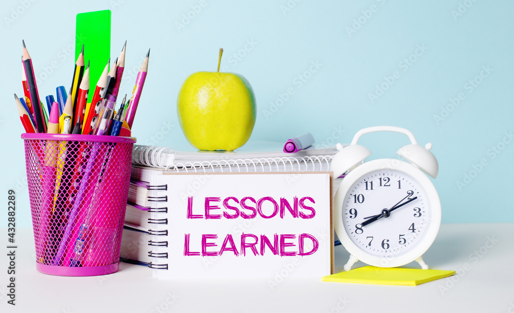 Poster on a light table there are books, stationery, a white alarm clock, an apple. next to it is a noteboo