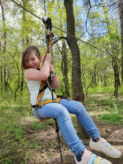Little Caucasian blond girl plays in the park or forest, rope park in outdoors. Summer sports children's activity and playing. Local vacation and tourism concept, the new normal reality covid-19