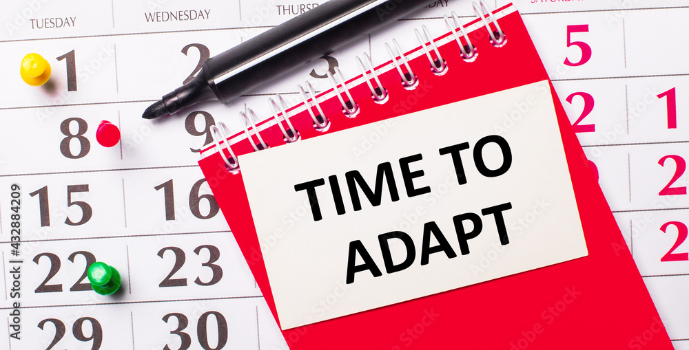 Poster on the calendar is a white card with the text time to adapt. nearby is a red notepad and a marker. v