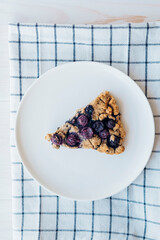 Piece of freshly baked oat blueberry scones on white plate, close up. Sweet food with natural ingredients. Vegan gluten free pastry.