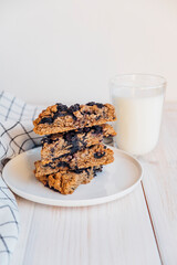 Stack of homemade oatmeal scones with berries stacked on white plate and glass of plant based milk. Vegan sweet baked food. Gluten free pastry. Healthy breakfast.