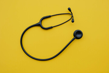 Black medical stethoscope on yellow background. Medicine and healthcare concept. Space for text. Flat-lay, top view.