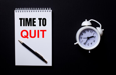 The words TIME TO QUIT is written in a white notepad near a white alarm clock on a black background.