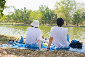 asian couple picnic and relax with happiness feeling in park with lake in springtime
