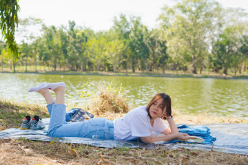 asian woman picnic and read book with happiness feeling in park with lake in springtime