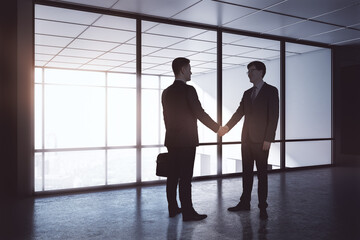 Fototapeta na wymiar Business deal and partnership concept with businessmen handshaking in dark spacious office in sunny morning.