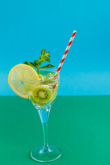 Kiwi cocktail garnished with lemon and mint in a glass on a napkin on a green background.