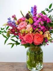 Spring flowers bouquet in a glass vase. Pink roses, carnations, and wildflowers. Fresh uplifting flora on white background.