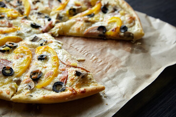 Pizza with chesse, ham, yellow bell pepper, olives and mushrooms on wooden table