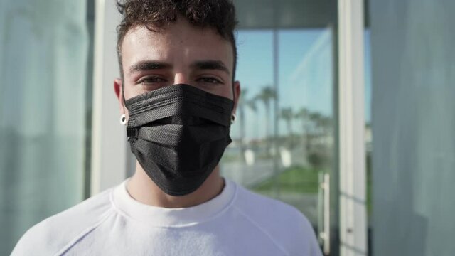 Young stylish man in a black Coronavirus protective mask looking at the camera, then pull it out and smiles. Concept of confidence in future for return to normal due to end of global Covid-19 pandemic