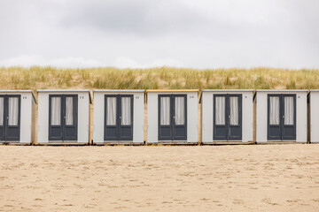 Graphic row of small closed square summer cubicle homes on Dutch North sea beach with dune behind on an overcast day 