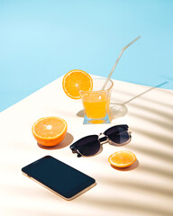 Summer tropical composition with yellow orange juice on the table with glasses and a phone for surfing. Shadow of a palm leaf on the table.