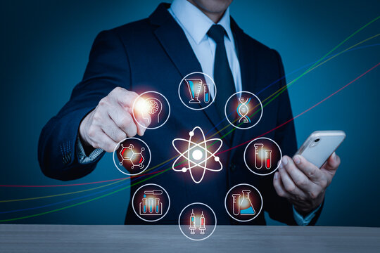 A man wearing a suit on his left hand holding a cell phone Right hand pointing to medical scientific icons such as syringe, test tube, DNA, brain x-ray, blurred background.