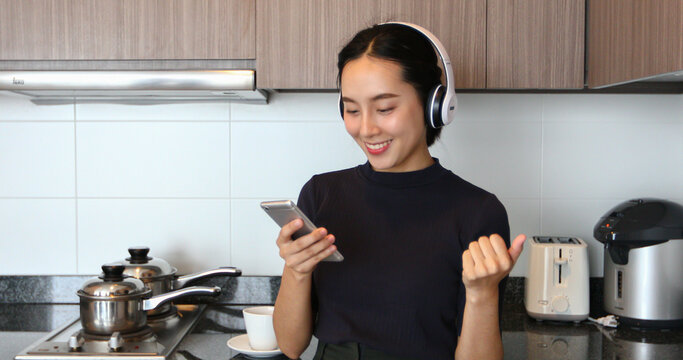 Asian women wearing headphone and listening to music in the kitchen at home