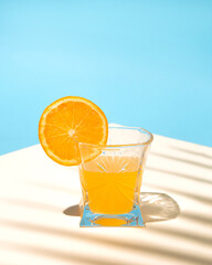 Summer tropical composition with yellow orange juice on the table with the shade of a palm leaf.