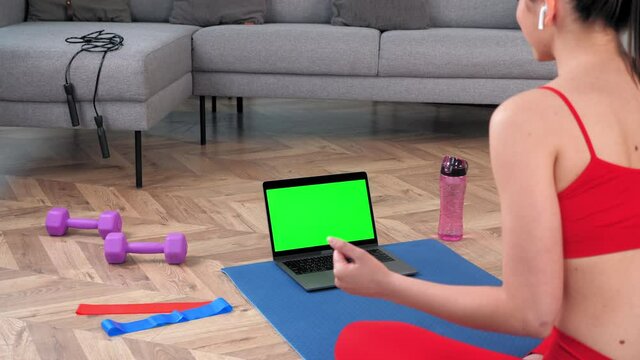 Green screen mock up chroma key monitor laptop concept: Emotional fit woman in sportswear sits on yoga mat looks computer display, tells fitness trainer online video call webcam, distance sport course