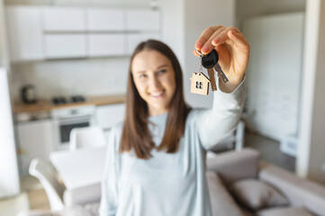 Selective focus on the key in hand of happy young woman, cheerful female moved in new house, rent...